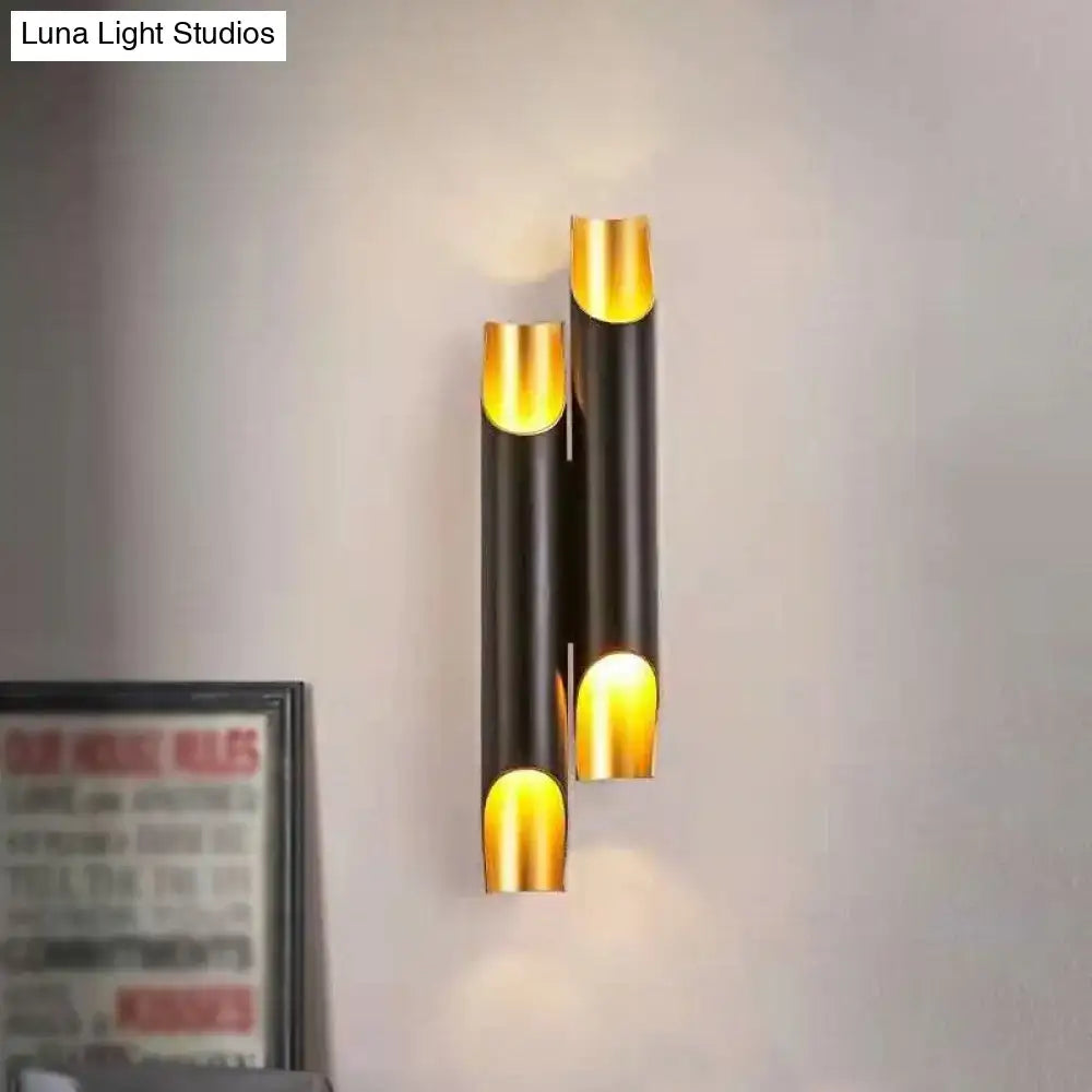 Modern white metal fixture wall sconce with gold accents and black cylindrical tubes emitting warm glow for living room