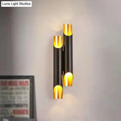 Modern white metal fixture wall sconce with gold accents and black cylindrical tubes emitting warm glow for living room