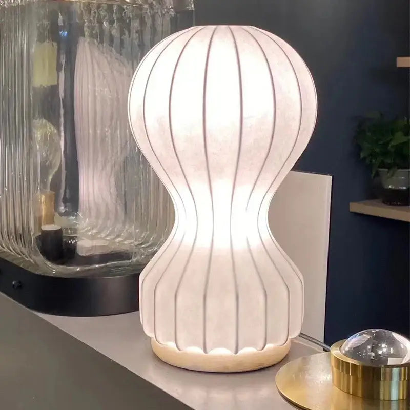 A modern white ribbed silk cocoon silk table lamp with rounded base softly glowing for bedroom decorbites gatto cocoon