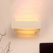 Modern white tiered rectangle wall lamp with layered stepped design emitting warm light for bedroom wall sconce use
