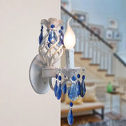 Modern white wall light with blue crystal draping featuring exposed bulb and dangling crystal droplets bedroom sconce