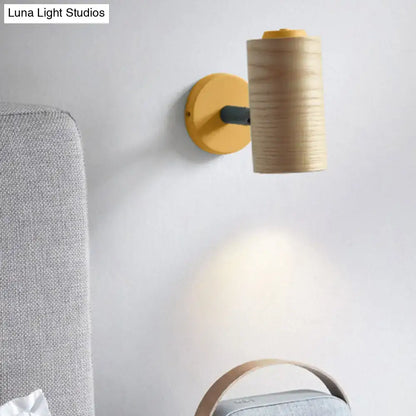 A modern wall-mounted lamp with a cylindrical wooden shade and yellow green metal base for bathroom use