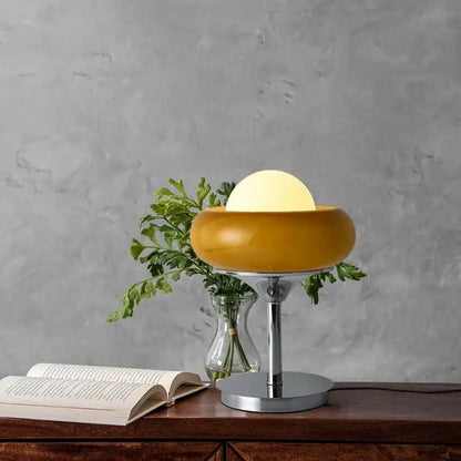 A sleek mustard-yellow glass egg tart desk lamp with chrome base and soft glowing bulb for modern bedroom use