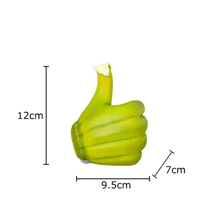 A lime green glossy plastic thumbs-up air freshener with white cap beside a modern yellow banana fist resin statue desk ornament
