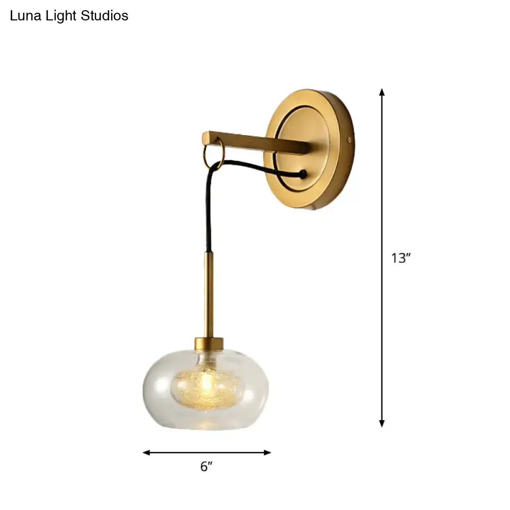 A sleek brass modernist amber white glass wall sconce with clear globe shade and exposed filament bulb for bedroom use