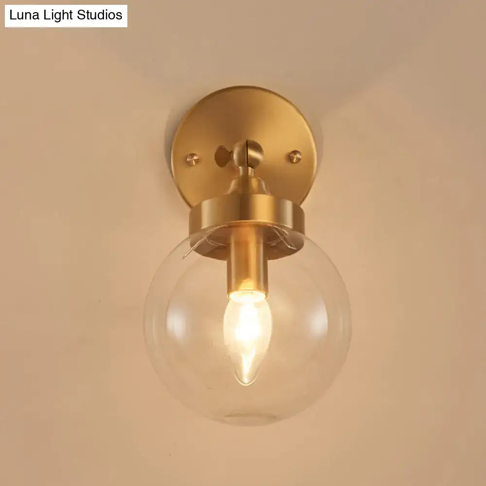 Brass-finished modernist ball wall lamp with clear glass globe and illuminated filament bulb wall mounted for bedroom