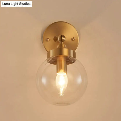 Brass-finished modernist ball wall lamp with clear glass globe and illuminated filament bulb wall mounted for bedroom