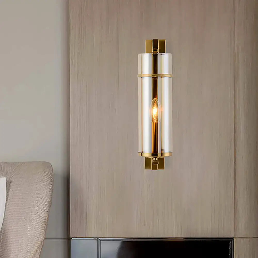 Modernist brass bedroom sconce light with sleek cylindrical design, polished gold metal accents, and frosted water blue glass panels