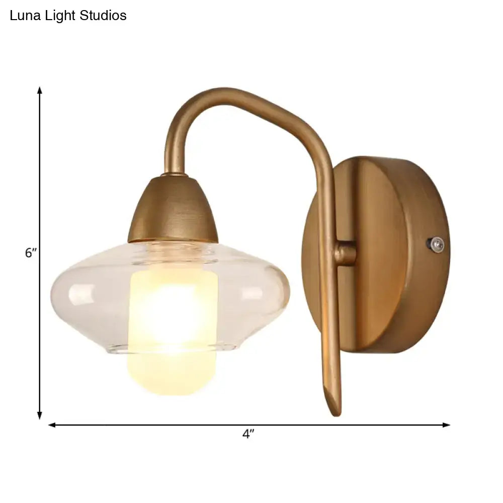 Modernist brass clear glass wall lamp with curved arm and bulb base designed as a bedroom sconce