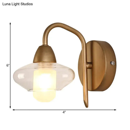 Modernist brass clear glass wall lamp with curved arm and bulb base designed as a bedroom sconce