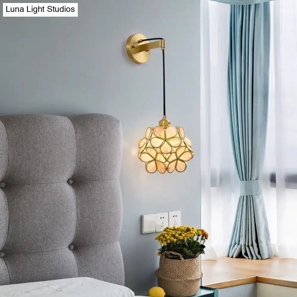 Modernist brass bulb bedside sconce with a gold-toned arm and a delicate light pink clear flower-shaped glass shade