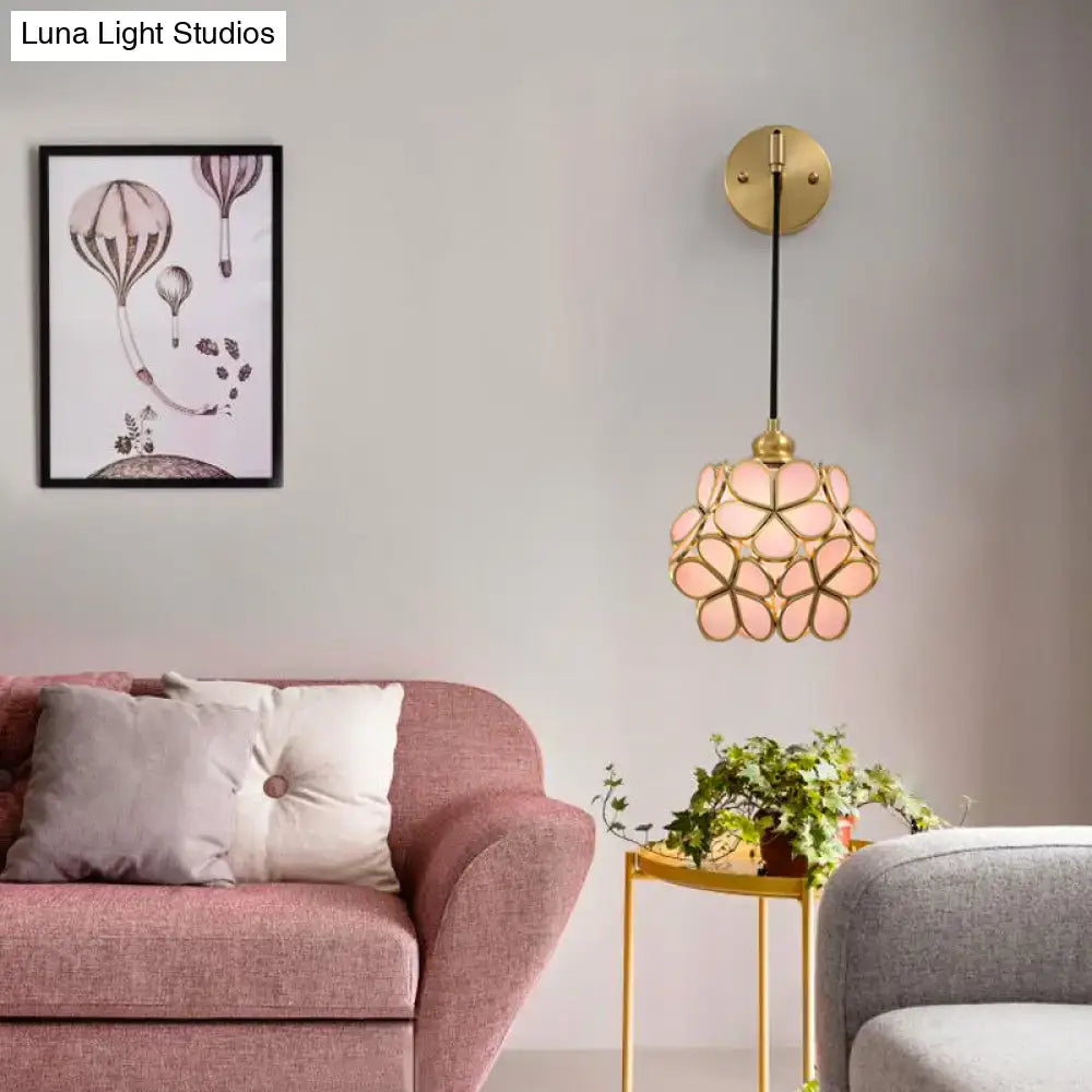 A light pink and clear bulb bedside sconce with a brass frame featuring a delicate floral glass pendant design