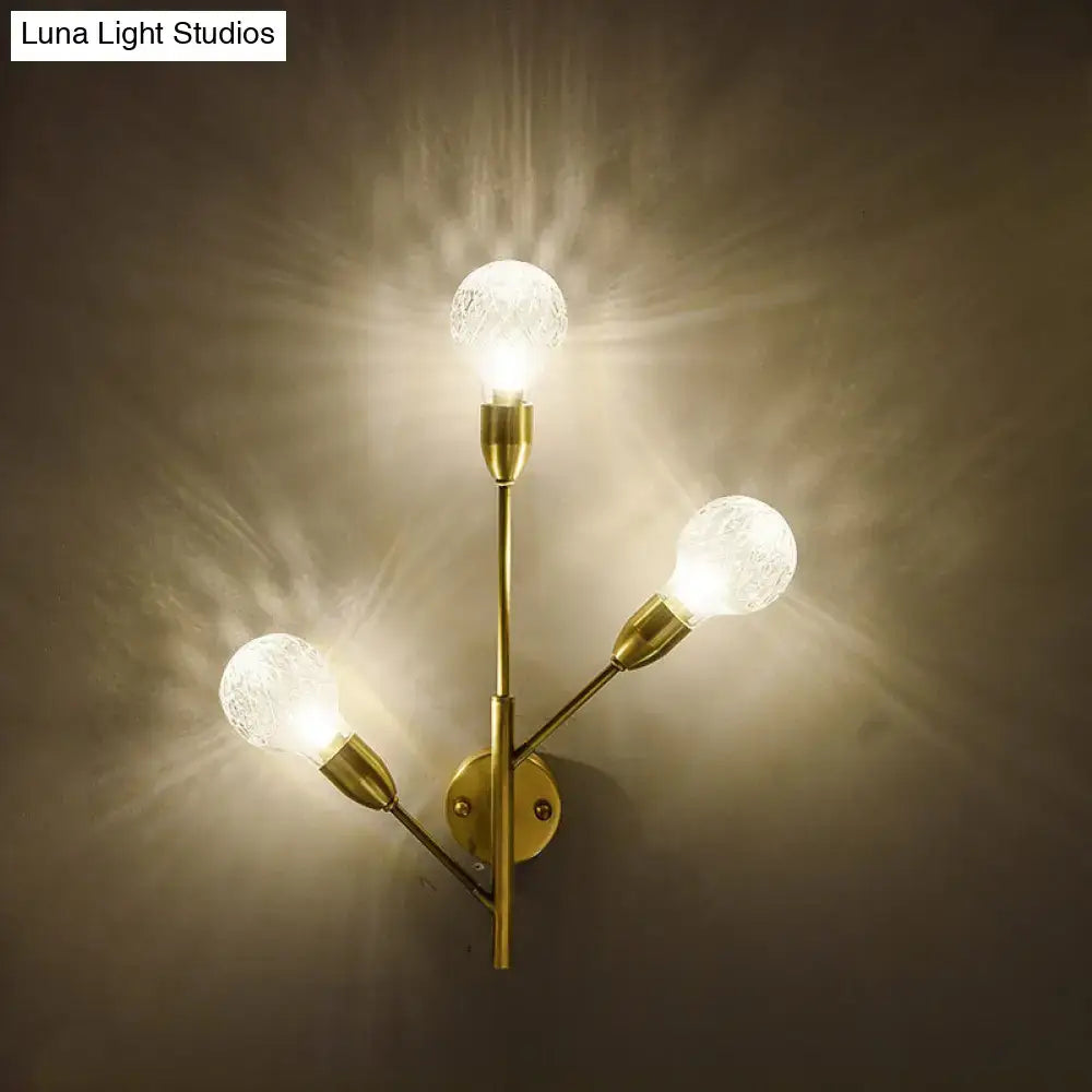 Modernist brass wall mount light fixture with three illuminated prismatic glass globe bulbs for bedroom use