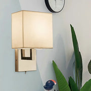 Modernist gold and beige sconce light fixture with gold-toned rectangular base and beige fabric shade for bedroom wall use