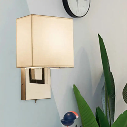 Modernist gold and beige sconce light fixture with gold-toned rectangular base and beige fabric shade for bedroom wall use
