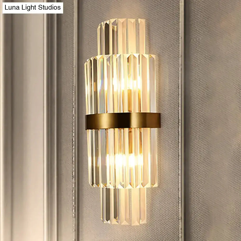 A modernist gold and clear crystal cylinder wall lighting fixture with vertical rods and a sleek brass band for living room