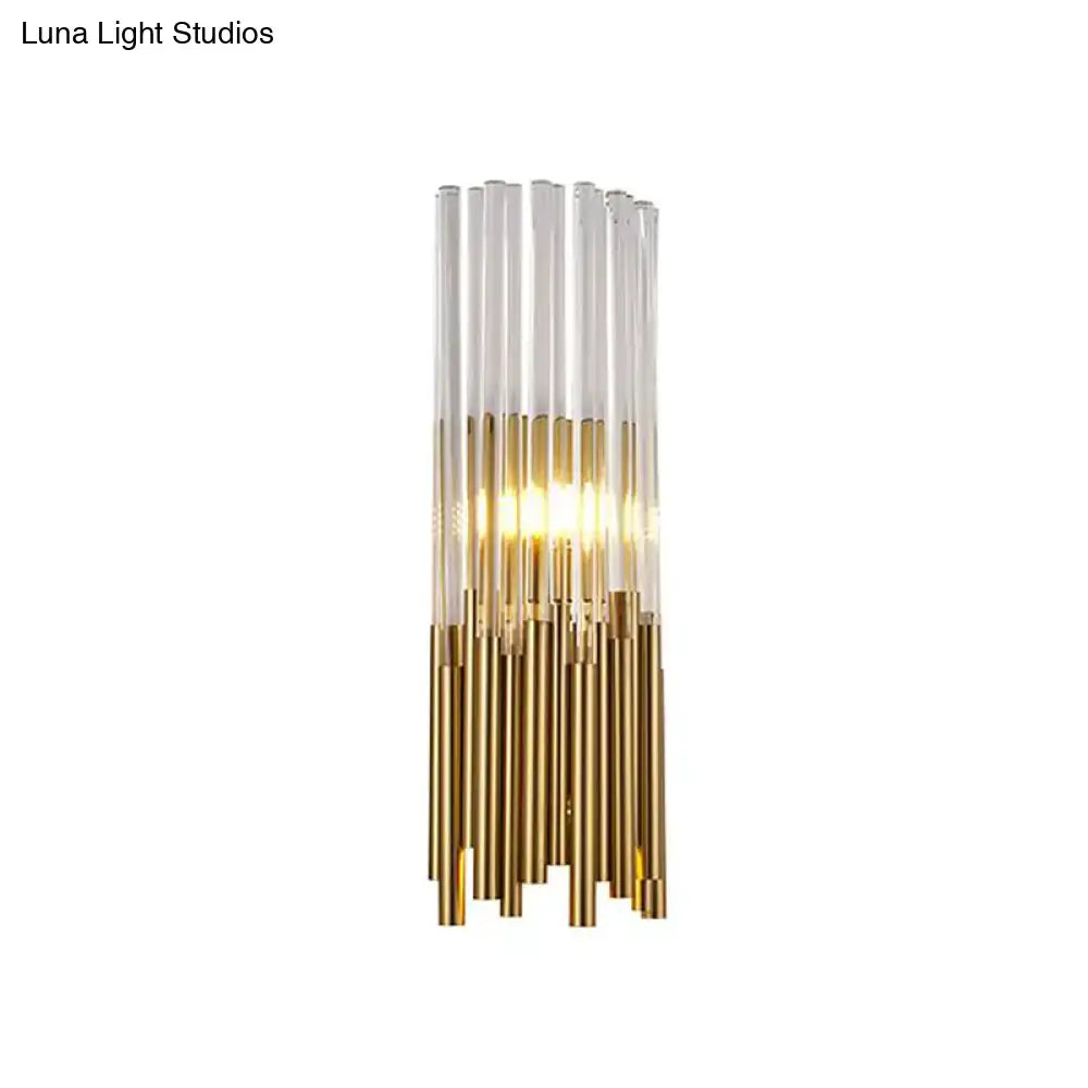 Modernist gold and clear cylinder wall light fixture with vertical glass tubes and warm glowing light for bedroom sconce