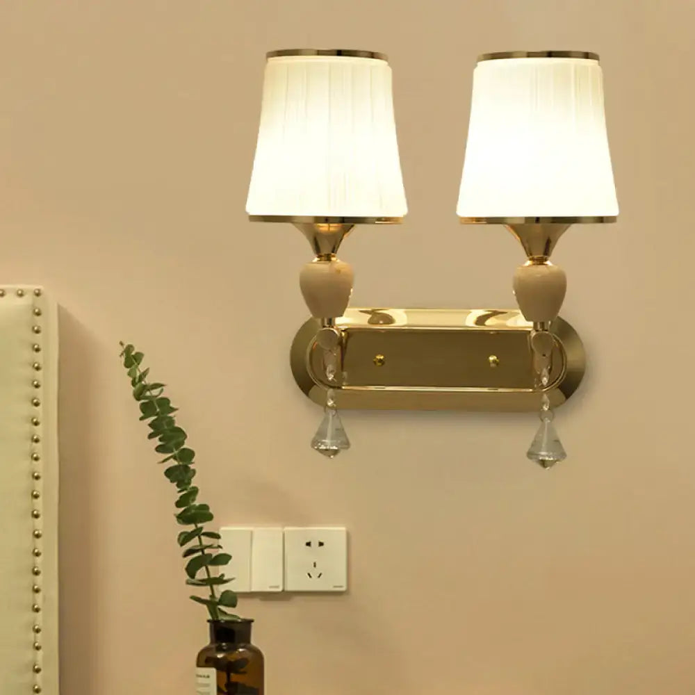 Modernist gold-toned crystal wall sconce with two white pleated lampshades for living room lighting