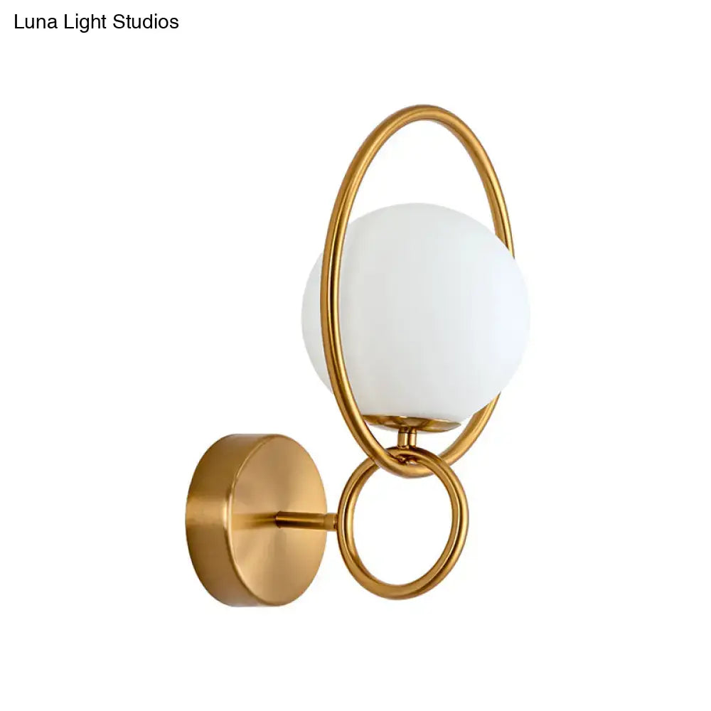 Modernist gold wall sconce featuring a white glass shade with frosted spherical globe and interlocking rings for bedroom
