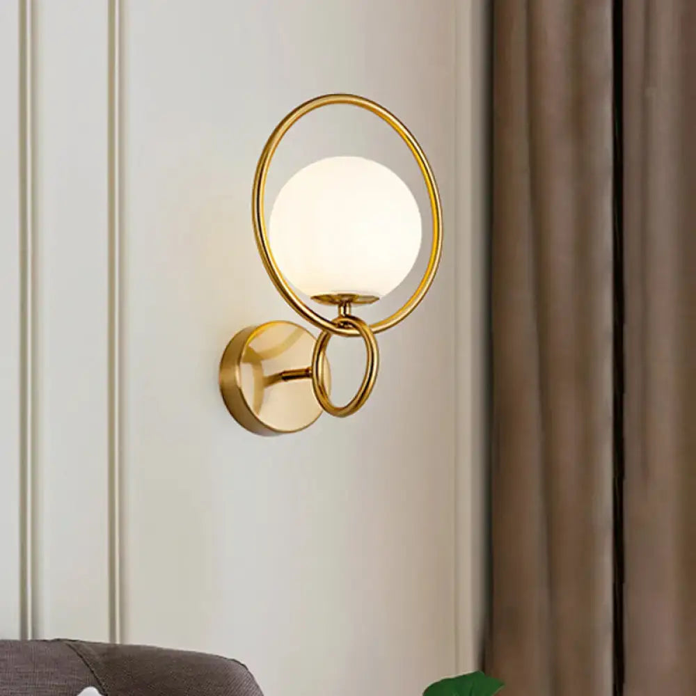 Modernist gold wall sconce with a circular frame and white glass shade for bedroom lighting
