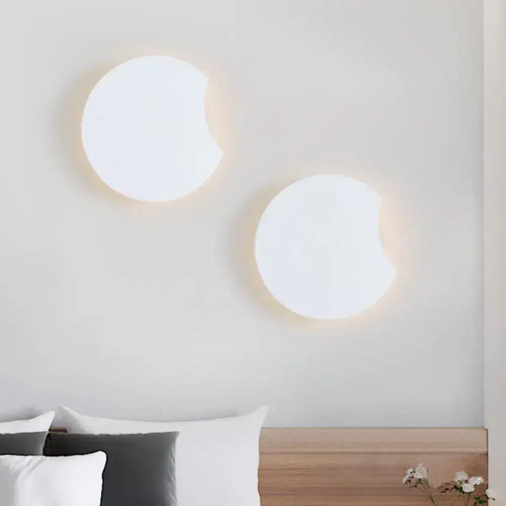 Modernist gray circular wall mount light with two minimalist white sconces emitting a warm glow for bedroom use
