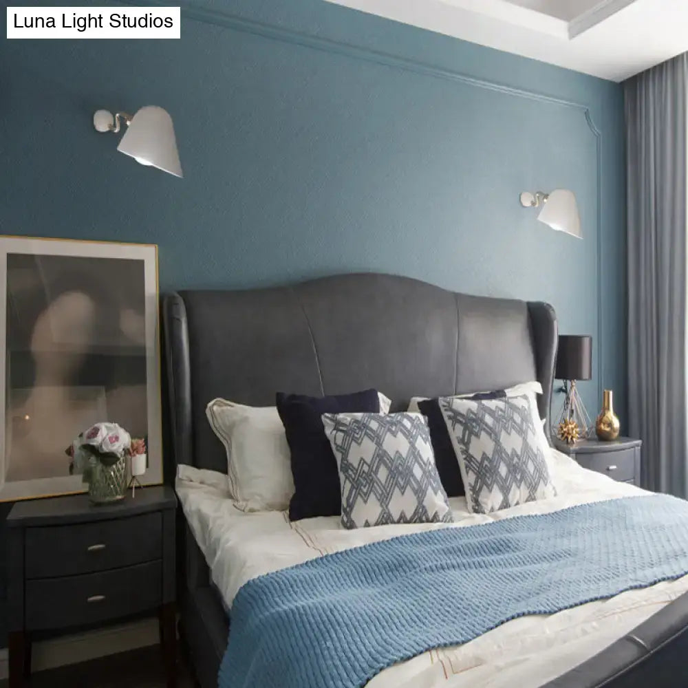 Black leather headboard with curved top and tufted design beneath modernist off-white and gold wall mounted sconce light with wide flare