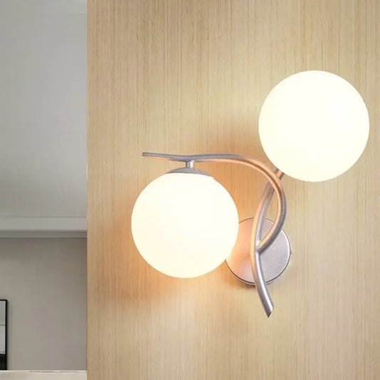 Modernist silver black two-light wall sconce with sleek metal arms and milky glass globe shades for bedroom use