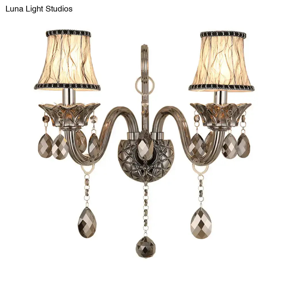 Antique brass two-light wall sconce with smoke grey faceted crystal droplets and beige lampshades for living room wall mounted lighting