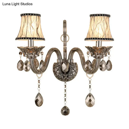 Antique brass two-light wall sconce with smoke grey faceted crystal droplets and beige lampshades for living room wall mounted lighting