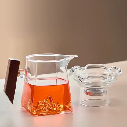 Clear glass tea cup set with dark wooden handle and intricate mountain base design filled with amber tea for dining room filter