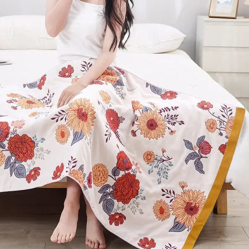 A multicolor gauze flower bath towel featuring a flowing white maxi skirt design with vibrant orange and red floral patterns and golden trim