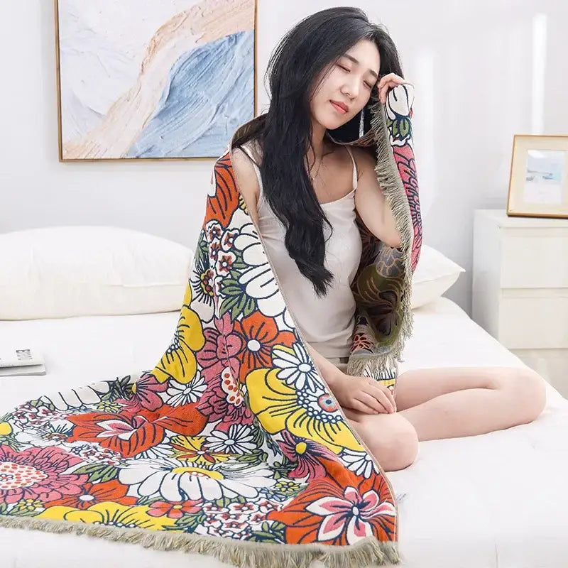 A vibrant multicolor decorbites gauze flower bath towel with fringe trim used as a bedroom floral throw blanket