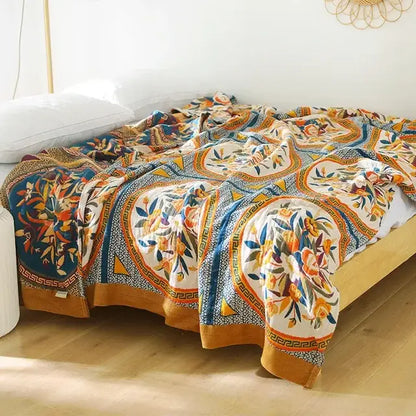A multicolored cotton gauze boho throw blanket with bold floral and geometric designs in orange blue teal and cream tones