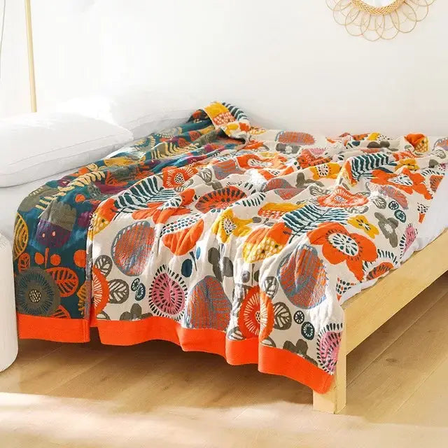 A multicolored cotton gauze boho throw blanket with bold orange and teal floral decorbites cotton gauze design on cream background