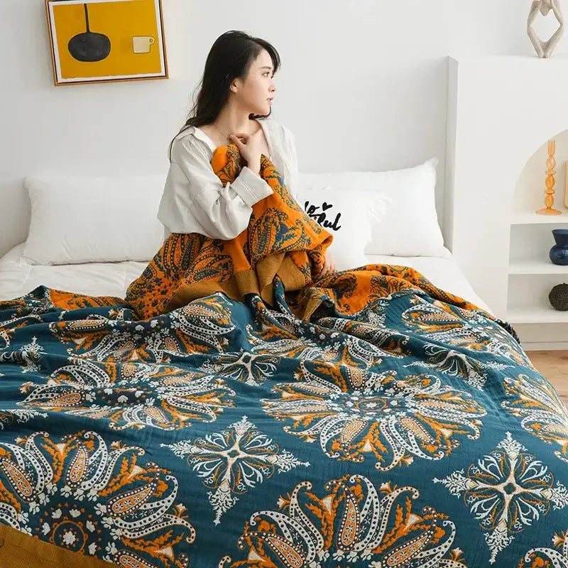 A cozy teal and orange paisley-patterned cotton gauze boho throw blanket draped over a woman in bed for decorbites cotton gauze