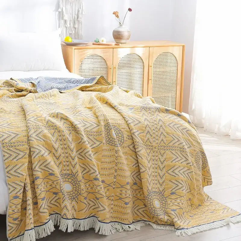 A soft yellow cotton gauze boho throw with gray and blue geometric patterns and white fringe for bedroom or living room decor