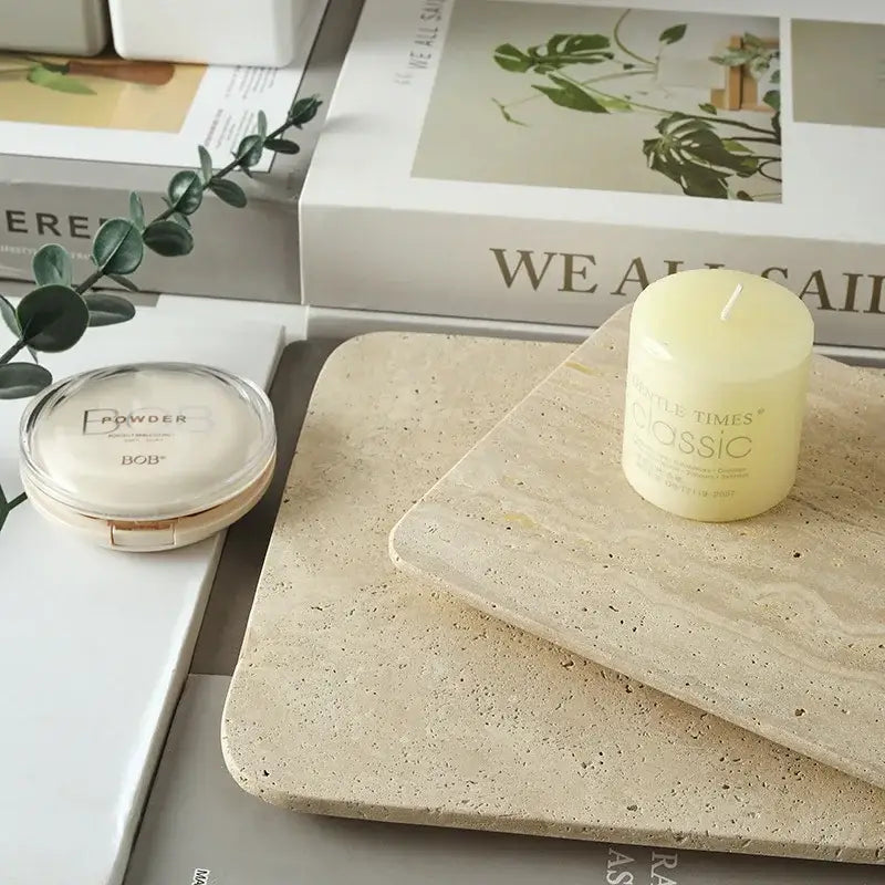 A pale yellow cylindrical candle on a decorbites beige travertine marble plate kitchen and bathroom tray