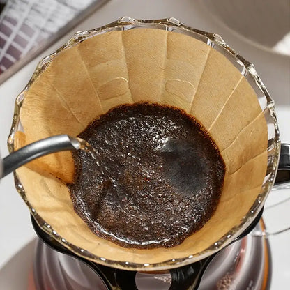Clear glass pour-over coffee dripper with natural brown cone coffee filter paper and dark wet coffee grounds inside filter papers decorbites coffee filter