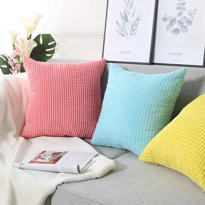 Three colorful decorbites corduroy corn grain cushion covers in pink light blue and yellow on a gray sofa