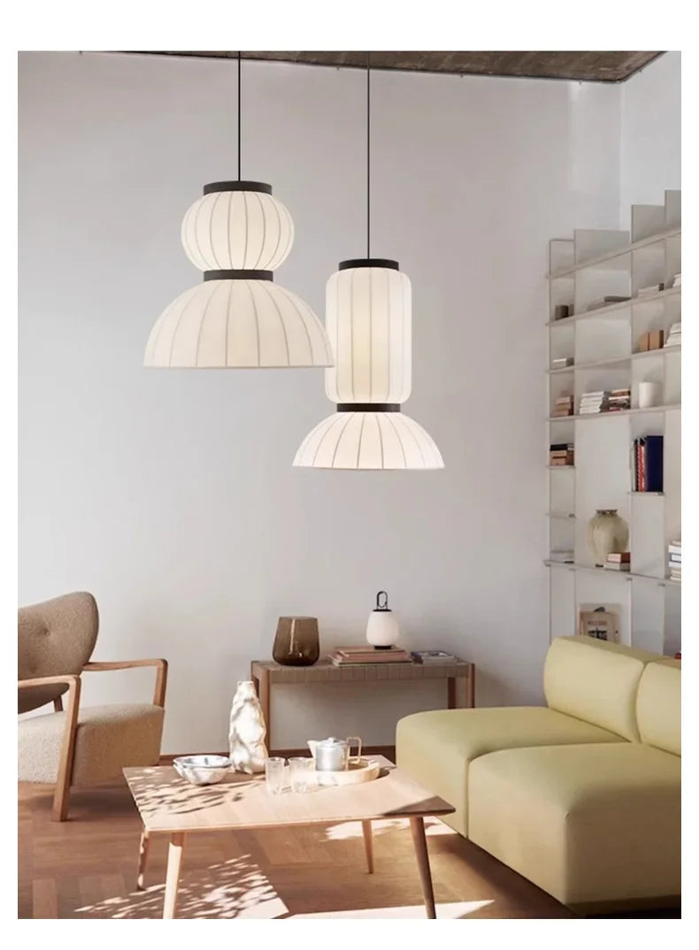 Two off-white pleated noguchi pendant lamps with black metal accents hang as dining room lantern light shop hanging light