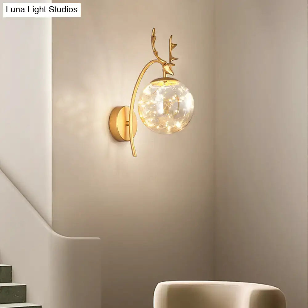Gold-toned nordic ball wall sconce with black antler mount and spherical glass globe housing warm led lights for bedroom