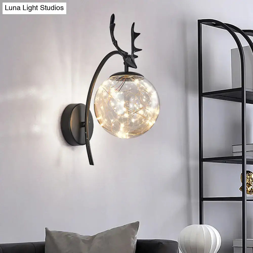Black metal nordic ball wall sconce with antler design and spherical glass globe housing warm fairy lights