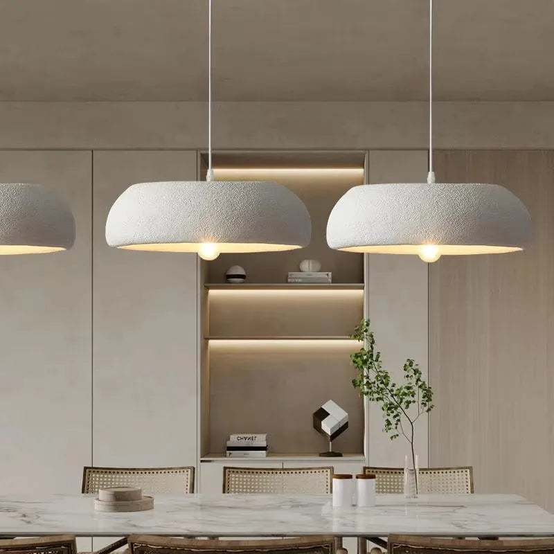 Three modern white ceramic pendant lamps with textured shades and warm led lighting above a marble dining table