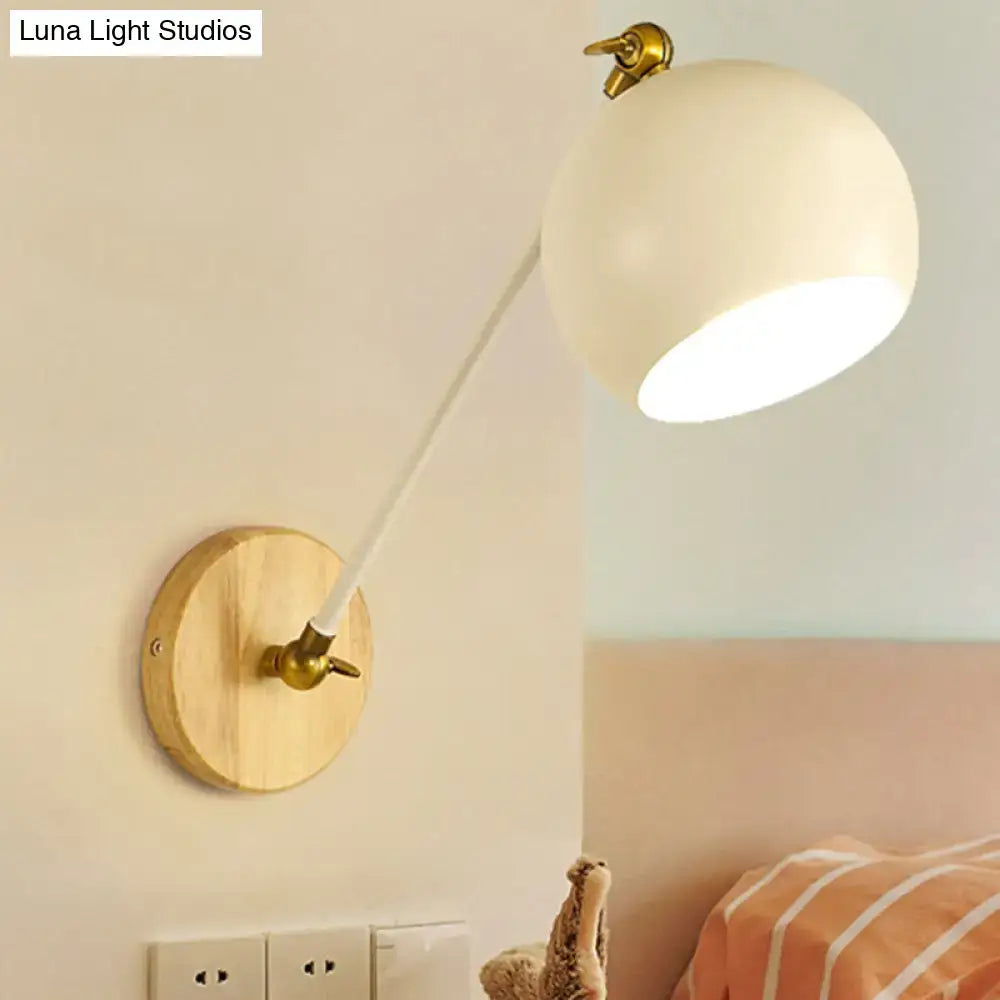 Cream-colored spherical wall light with brass-finished adjustable arm wooden base and bulb socket for bedroom use