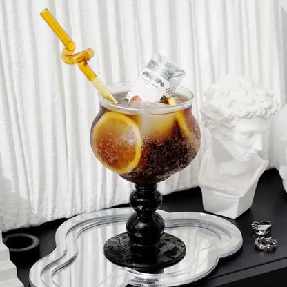 A tall nordic black glass beaded stem goblet filled with iced coffee and garnished with orange slices for stylish decorbites use