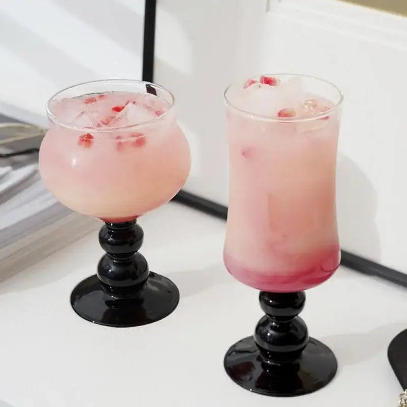 Two elegant black nordic black glass beaded stem goblets filled with pink beverage and ice cubes for kitchen use