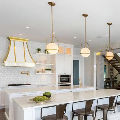 Three elegant nordic brass glass globe pendant lights with frosted shades hang above a modern kitchen island