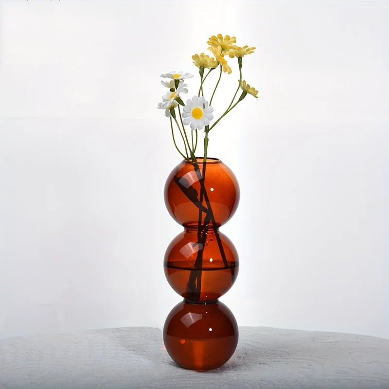 A translucent amber glass nordic bubble vase with three spherical sections holding white and yellow daisies