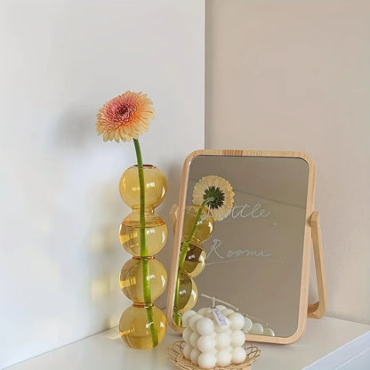 A tall translucent amber glass Nordic bubble vase with stacked spheres holds a pink and yellow gerbera daisy