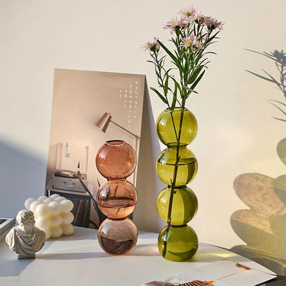 A tall translucent green glass Nordic glass bubble vase with stacked spheres holding delicate purple flowers